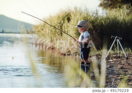 A small toddler boy standing by a lake at sunset, fishing. Copy space. 49170229