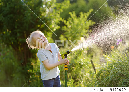 Funny little boy playing with garden hose in sunny 49175099