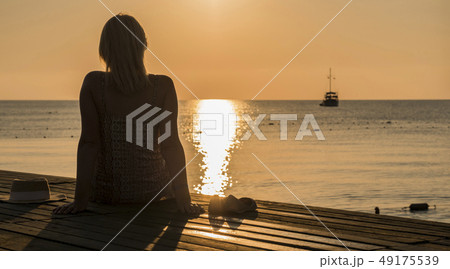 Rear view of a young woman admiring the dawn of the sea, in the distance a ship is visible. Romance Rear view of a young woman admiring the dawn of the sea, in the distance a ship is visible. Romance 49175539
