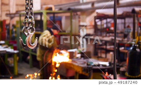 Construction plant. A big industrial lifting chain with a hook on the end. A man welding on the Construction plant. A big industrial lifting chain with a hook on the end. A man welding on the 49187240