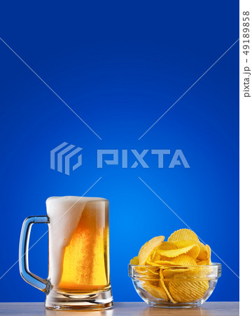 Mug of light beer with foam and chips on blue background 49189858