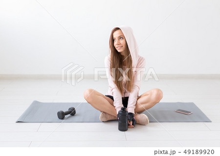 Fitness, sport, people concept - young woman is sitting on the mat after an exercise and looking Fitness, sport, people concept - young woman is sitting on the mat after an exercise and looking 49189920