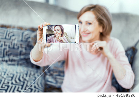 Elderly Woman With a Phone in Her Hands in Good Mood is Resting at Home in the Living Room. 49199530
