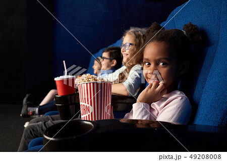 Cute girl sitting in cinema with friends, looking at camera. 49208008