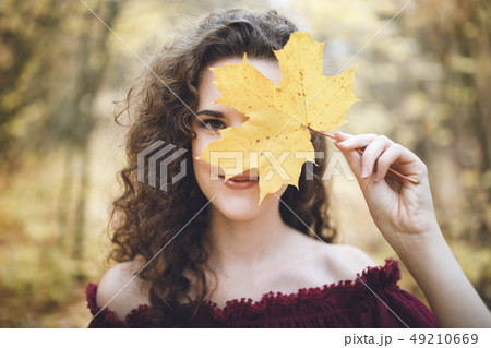 Happy girl in an atumn park holding maple leaf in 49210669