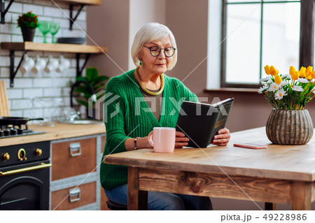Septuagenarian silver-haired looking through Bible book sitting at kitchen table Septuagenarian silver-haired looking through Bible book sitting at kitchen table 49228986