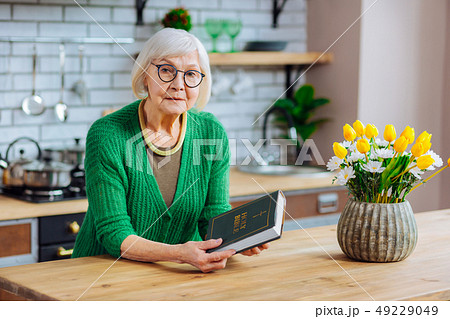 Beautiful grey-haired woman holding a Holy Bible book at kitchen Beautiful grey-haired woman holding a Holy Bible book at kitchen 49229049
