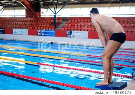 Muscular swimmer preparing to jump from starting block in a swimming pool 49230176
