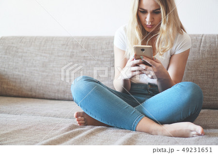 Attractive young woman relaxing on a sofa at home and using smart phone Attractive young woman relaxing on a sofa at home and using smart phone 49231651
