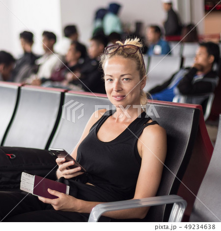 Casual tanned blond female traveler holding cell phone, passport and boarding pass while waiting to Casual tanned blond female traveler holding cell phone, passport and boarding pass while waiting to 49234638