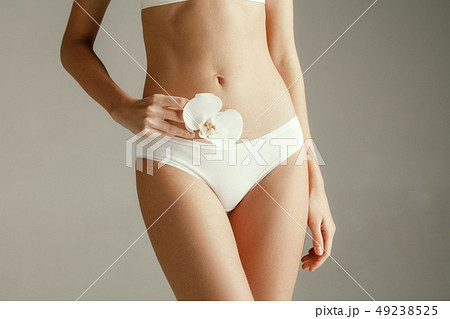 Young woman with epilated bikini zone holding flower on light background Young woman with epilated bikini zone holding flower on light background 49238525