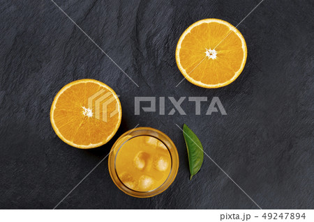 Fresh orange juice with orange halves and a green leaf, shot from above on a black background with 49247894