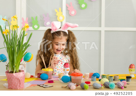 little child girl with Easter bunny ears painting Easter eggs at home. little child girl with Easter bunny ears painting Easter eggs at home. 49252205