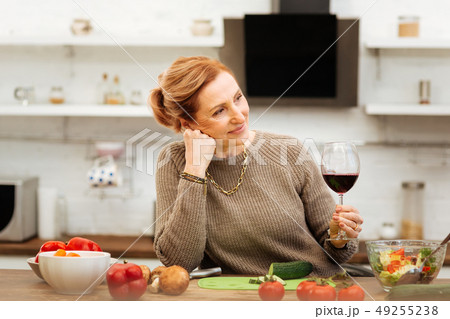 Pleasant ginger mature woman wearing sweater while staying in kitchen alone Pleasant ginger mature woman wearing sweater while staying in kitchen alone 49255238
