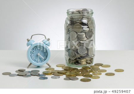alarm clock and coins in glass jar on wooden desk 49259407