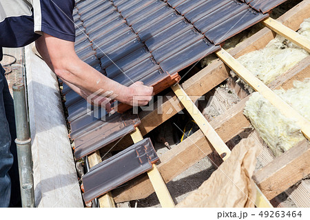 a roofer laying tile on the roof 49263464