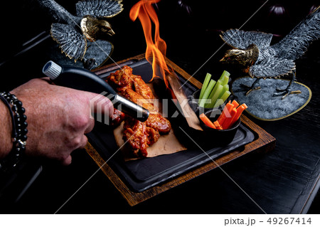 Delicious pieces of chicken wings grilled with Fire flames. On restaurant black background. Barbecue 49267414