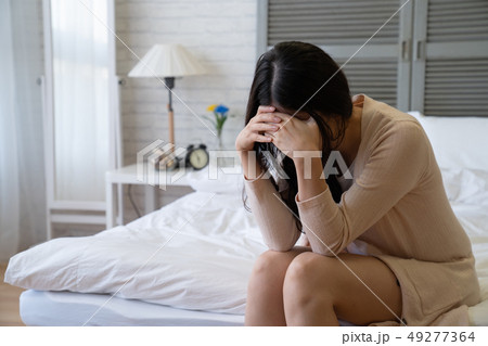 ill young woman sitting on bed covering face 49277364