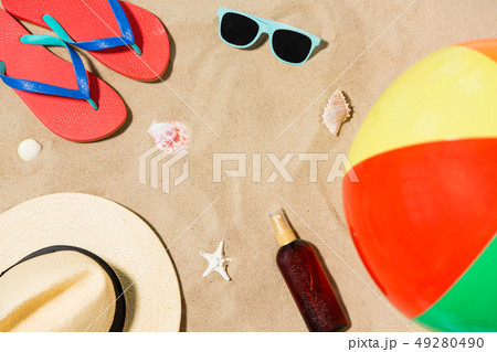 hat, flip flops and shades and beach ball on sand 49280490