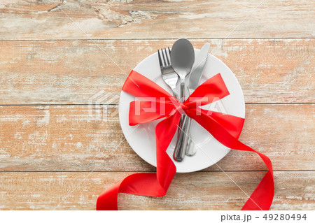 cutlery tied with red ribbon on set of plates 49280494