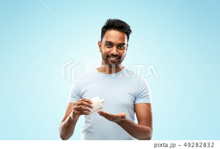 happy indian man applying lotion to his hand 49282832