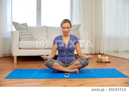 woman with music on smartphone meditating at home woman with music on smartphone meditating at home 49283518