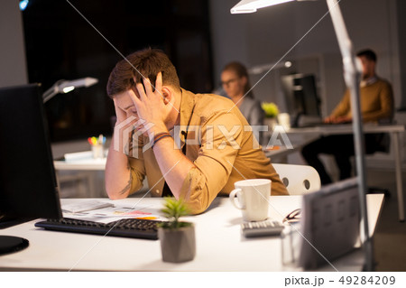 stressed man at computer monitor at night office stressed man at computer monitor at night office 49284209