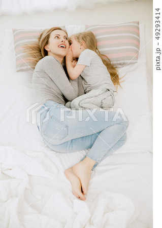 Young mother and her little daughter hugging and kissing on bed Young mother and her little daughter hugging and kissing on bed 49293414