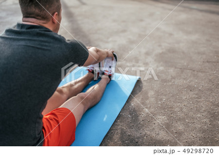 A male athlete doing gymnastics on mat, stretching muscles, training summer city on sports field A male athlete doing gymnastics on mat, stretching muscles, training summer city on sports field 49298720