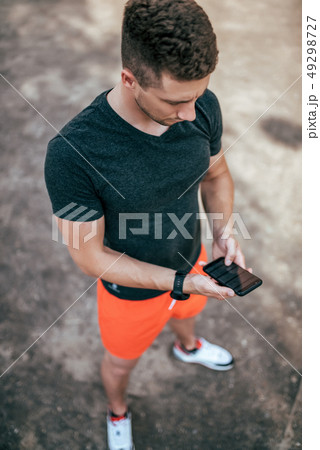 A male athlete, summer city on sports field, holds phone in his hand, a choice of Internet 49298727