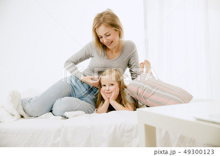 Young mother and her little daughter hugging and kissing on bed Young mother and her little daughter hugging and kissing on bed 49300123
