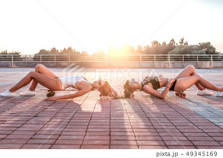 Two girls girlfriends, relax weekends, white black body lies on skateboard in summer city, longboard 49345169