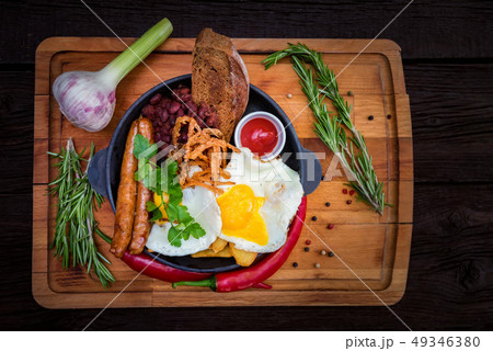 Nutricious meal with fried egg, sausages, beans, onion rings, chili pepper Nutricious meal with fried egg, sausages, beans, onion rings, chili pepper 49346380
