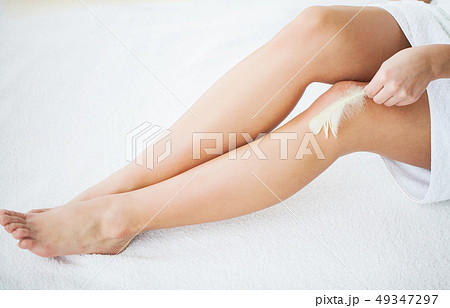 Skin Care and Health. Hair Removal. Woman With Feather Touching Bare Legs On Bed Skin Care and Health. Hair Removal. Woman With Feather Touching Bare Legs On Bed 49347297