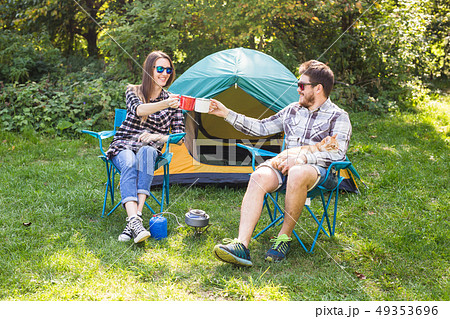 people, summer tourism and nature concept - young couple sitting near a tent 49353696