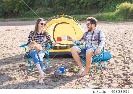 people, summer tourism and nature concept - young couple drinking tea near tent people, summer tourism and nature concept - young couple drinking tea near tent 49353935