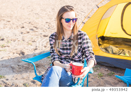 people, summer tourism and nature concept - young woman sitting near tent 49353942