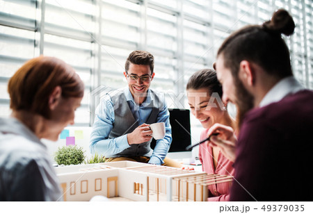 Group of young architects with model of a house working in office, talking. 49379035