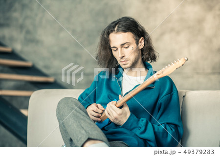 Curious young man with tattoo in his cheek setting up musical instrument 49379283