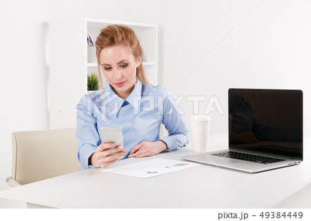 Photo of a nice office girl using phone near the laptop at her workplace. 49384449