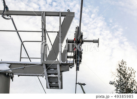 Steel ropes over wheels in mechanism on top of ski chair lift support pillar, bright sky background 49385985