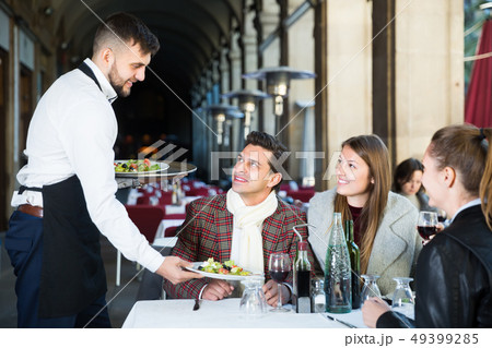 polite waiter serving guests at terrace restaurant 49399285