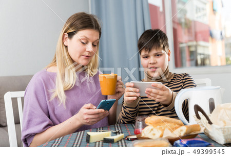 Portrait of young mother and son using phones during breakfast Portrait of young mother and son using phones during breakfast 49399545