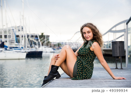 Sexy girl in dress sitting at quay with boats on background in Barcelona 49399934