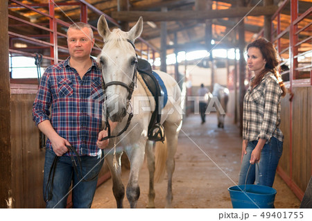 Couple of farmers with bucket before horse standing at stabling Couple of farmers with bucket before horse standing at stabling 49401755
