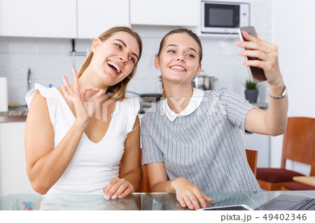 Two young girlfriends making selfie by phone and smiling at table Two young girlfriends making selfie by phone and smiling at table 49402346