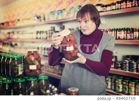 Woman consumer choosing glass jar of tomatoes Woman consumer choosing glass jar of tomatoes 49402710