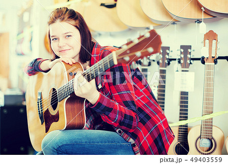 Сheerful teen girl examining various acoustic guitars 49403559