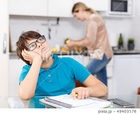 Boy doing homework, mother cooking Boy doing homework, mother cooking 49403576