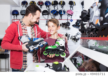 father and son deciding on new roller-skates in sports store father and son deciding on new roller-skates in sports store 49403711